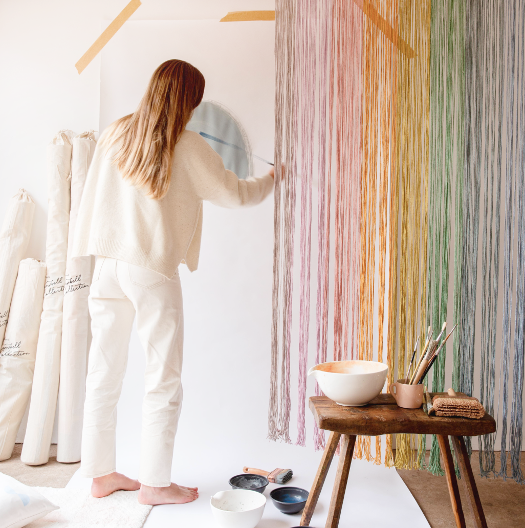  A woman wearing a white jumper and skirt, drawing watercolour paint on a wall.