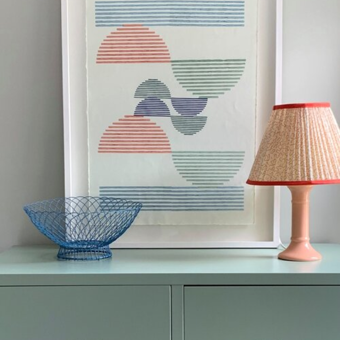  A drawing art in a white frame, an orange lamp and blue fruit basket