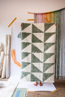  A person holding up a rug with a green and cream triangle pattern 