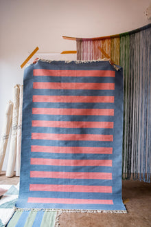  A person holding up a rug with a blue background and pink stripes on