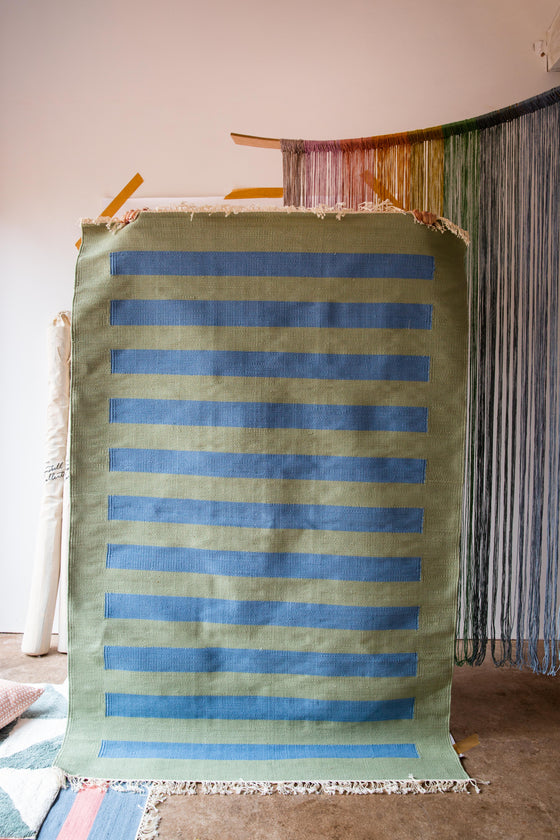A person holding up a rug with a green background and blue stripes on