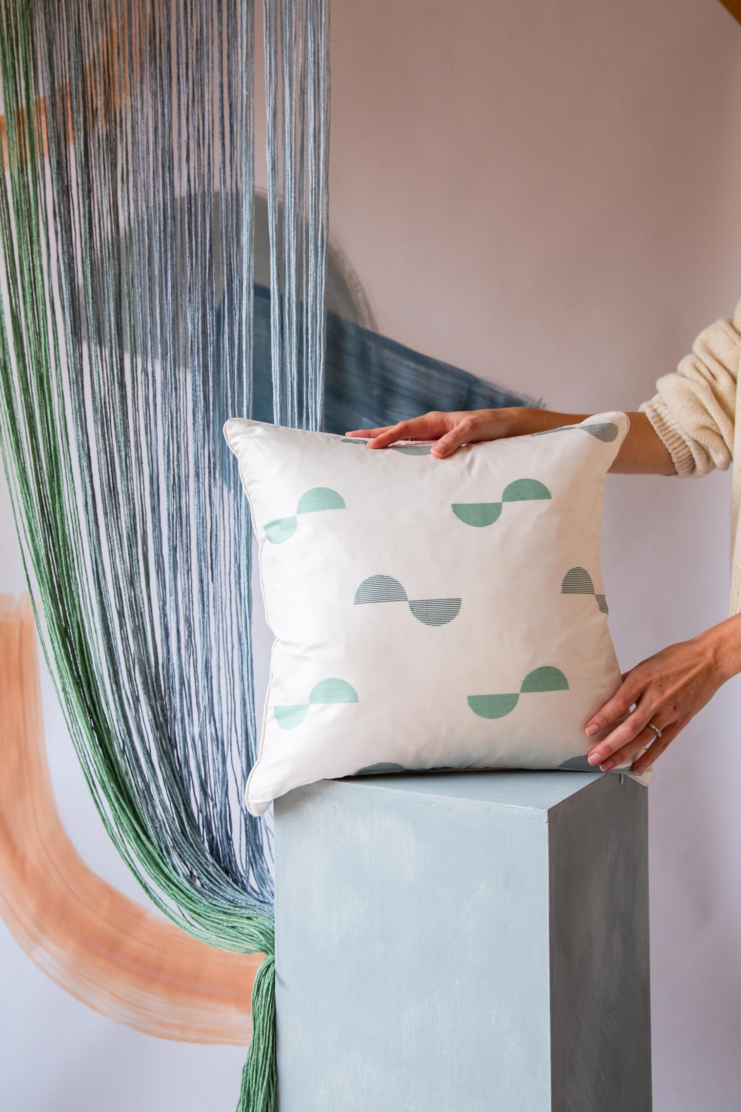 Someone holding a square cream colored cushion with green spots on