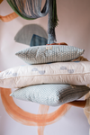 Someone holding a pile of three cushions. The top and bottom cushion are blue with a triangle pattern on and the middle cushion is cream with blue spots on