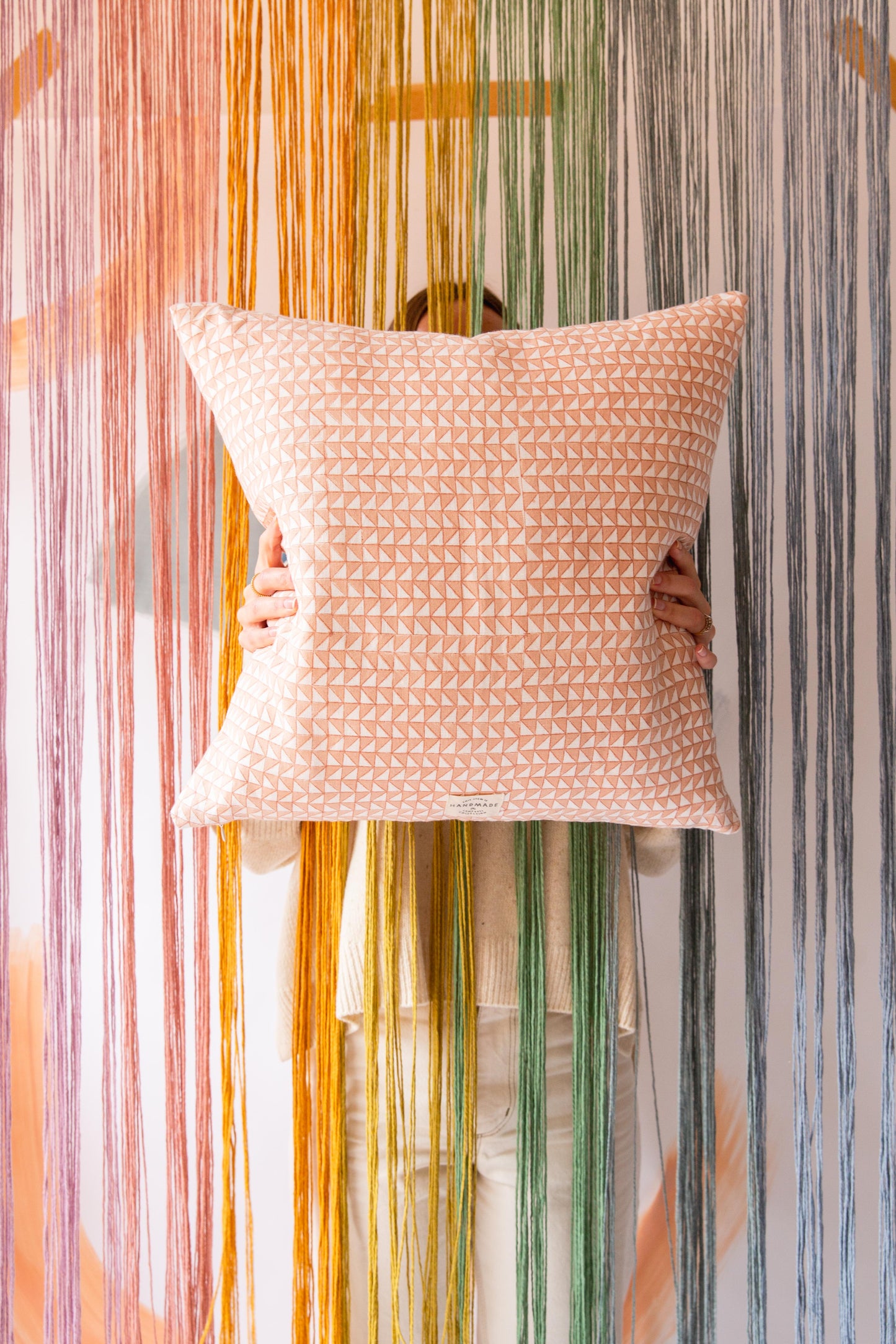 Someone holding a pink square cushion with a triangle pattern on