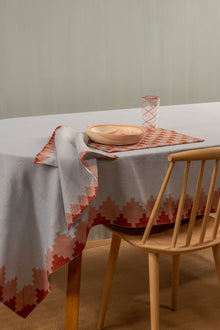  Blue napkin with red trim next to a place setting for one, on a table covered with table cloth