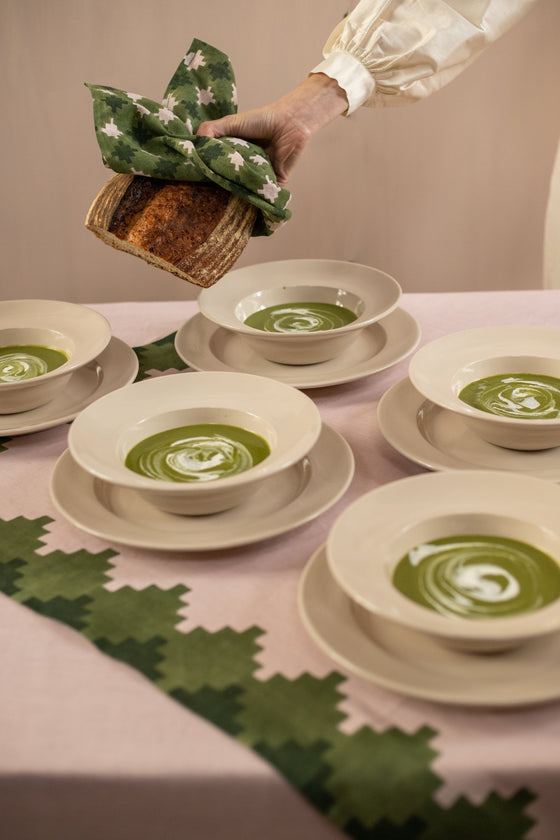 Pink tablecloth with green trim under five bowls of green soup