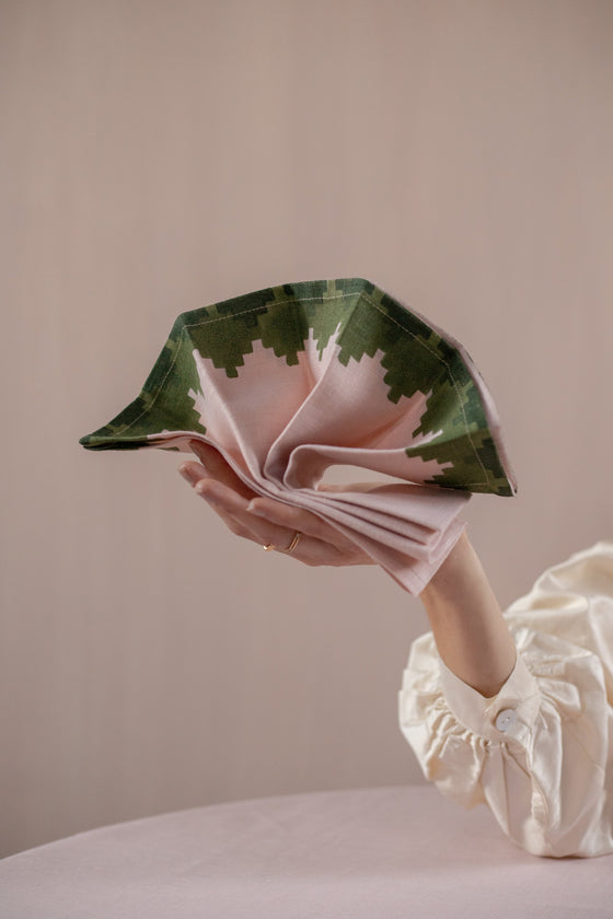 Hand holding a partially folded pink napkin with green trim