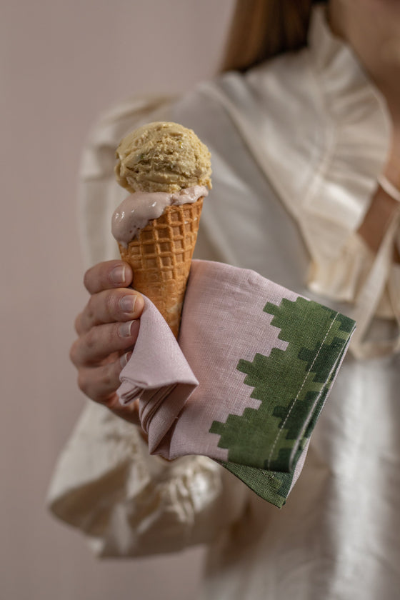 Hand using a pink napkin with green trim to hold an ice cream cone