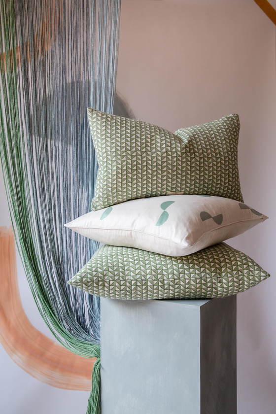 A pile of three cushions, the top and bottom have a green and cream pattern and the middle cushion is cream with green dots on