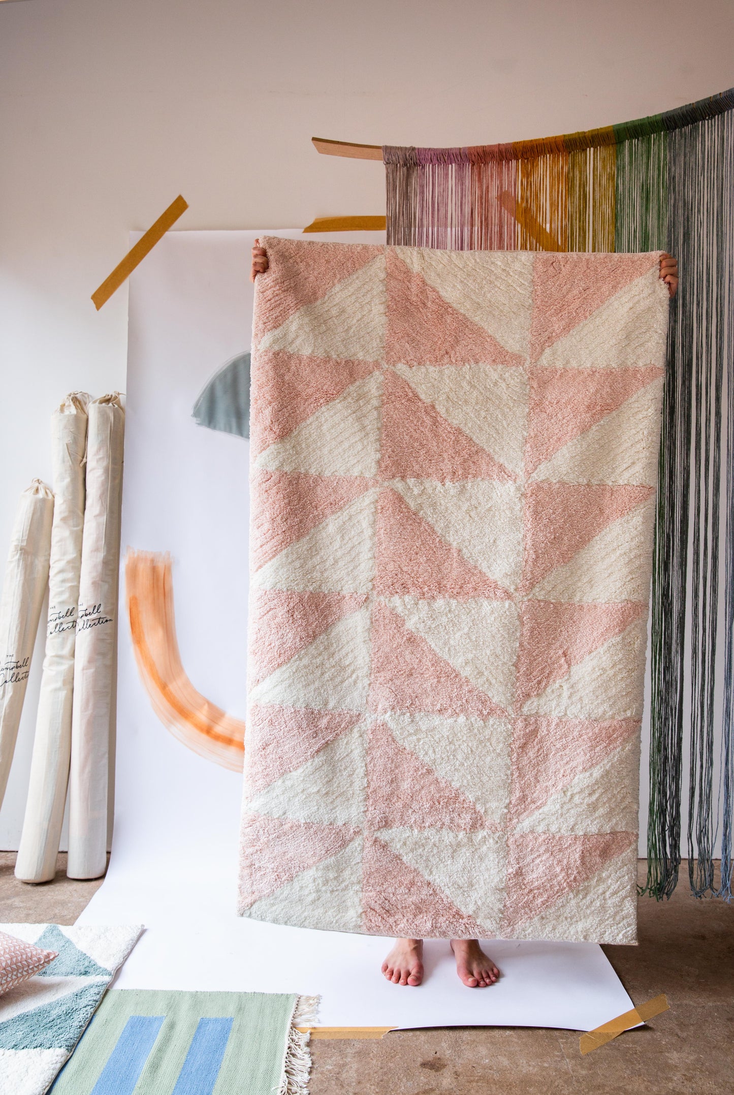 A person holding up a rug with a pink and cream triangle pattern on